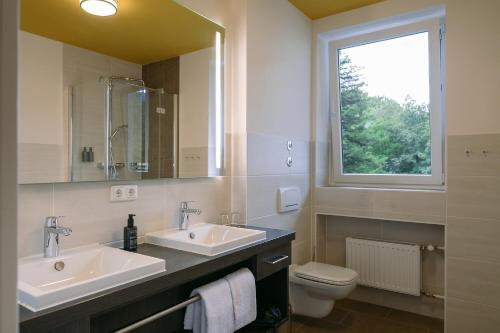 a bathroom with two sinks and a toilet and a window at HENRI Hotel Garmisch-Partenkirchen in Garmisch-Partenkirchen