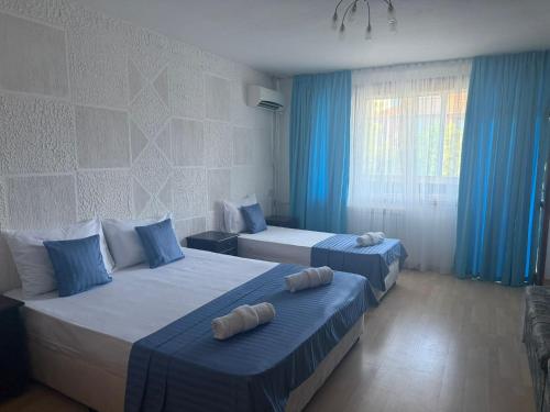 a hotel room with two beds with blue curtains at Къща за гости Стил in Kiten
