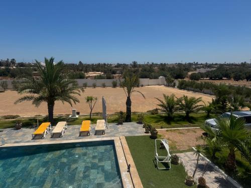 a swimming pool with lounge chairs and palm trees at Dar amiratou in Djerba