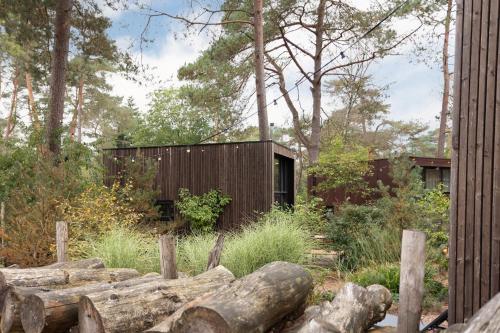 a house in the woods with a fence and logs at Tiny House of Happiness - shared hot tub in Otterlo