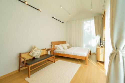 a bedroom with a bed and a bench and a window at After Beach House Phla Resort in U-Tapao