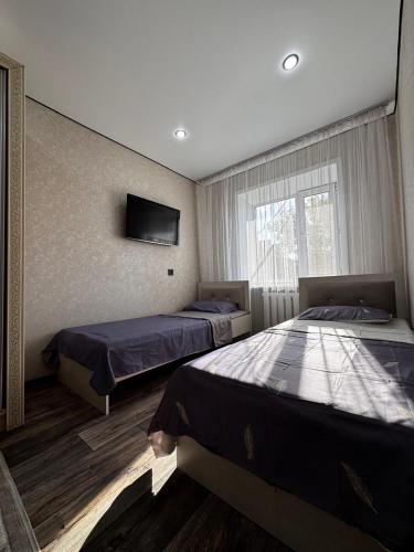 a bedroom with two beds and a tv on the wall at Квартира in Temirtaū