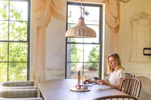 a woman sitting at a table looking at her cell phone at Maison Foxglove - Petite Acres Chateau in New Buffalo