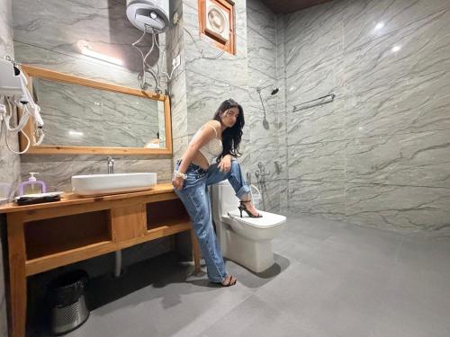 a woman is sitting on a toilet in a bathroom at Tirthan Wood , a river view cottage in Banjār