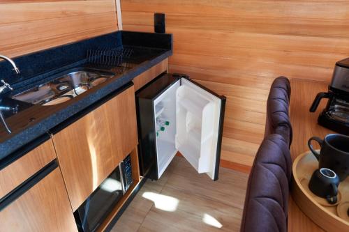 an open refrigerator in a kitchen with a sink at Encantos de Altitude Cabanas e Studio Container in São Joaquim
