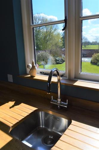a kitchen sink with a cat sitting on a window sill at Cockloft Romantic Countryside Hideaway in Bishops Cannings