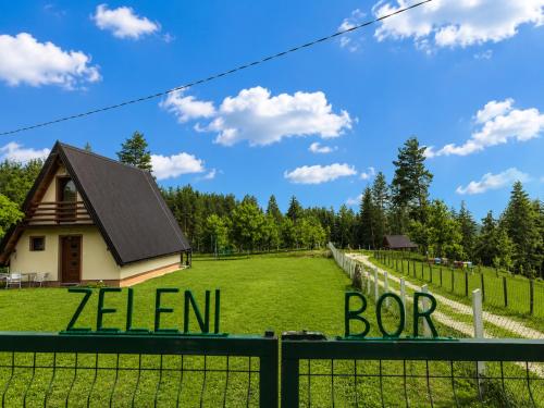 a house in a field behind a fence with a sign at ZELENI BOR koliba vikendica Pale in Pale