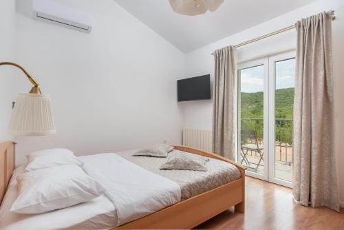 a white bedroom with a bed and a large window at Villa Sky Stone, Heated Pool, Playground in Krstatice