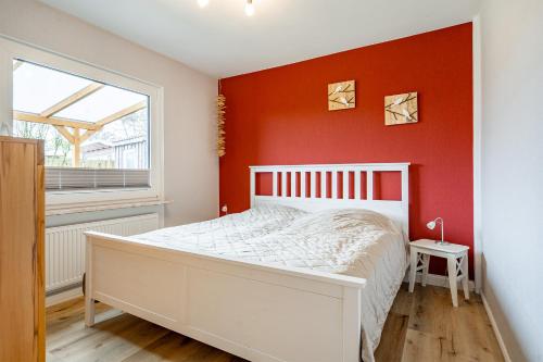 a bedroom with a white bed and a red wall at Bungalow Hohes Riff in Norddeich