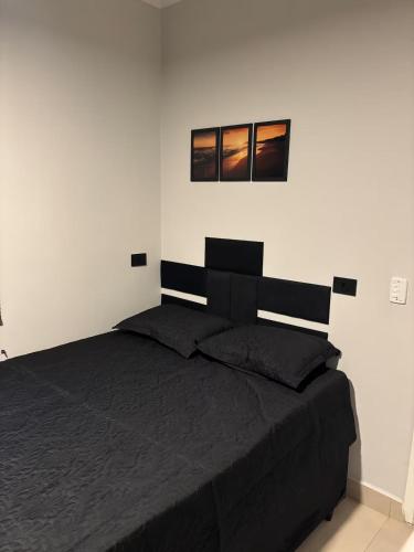 a bedroom with a black bed with two pictures on the wall at Sussurros do Mar in Bertioga