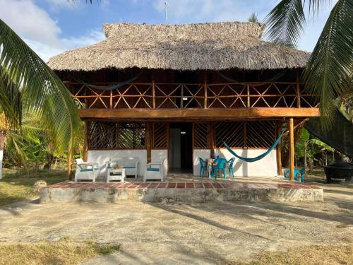 a house with a thatched roof with chairs and tables at Villa Neluc in San Bernardo del Viento