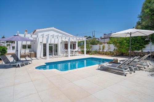 a pool with chairs and umbrellas next to a house at Villa de Amigos in Cala en Porter