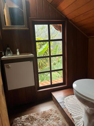 a bathroom with a window and a white toilet at Chalé Lumiar M&C in Lumiar