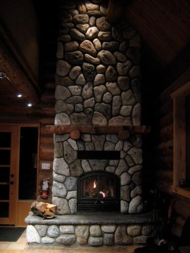 a stone fireplace with a fire in a room at Handsome Dan's at Otter Point in Sooke