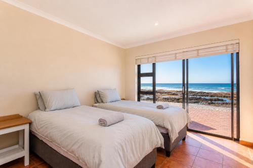 two beds in a room with a view of the ocean at High Tide Seafront at Franskraal in Franskraalstrand