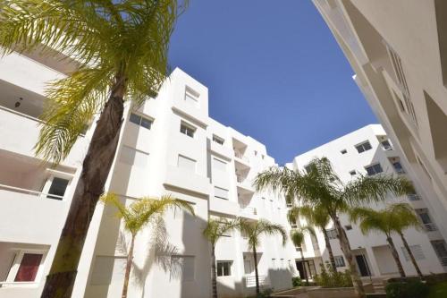 a white building with palm trees in front of it at Super Appartement à Bouznika in Bouznika