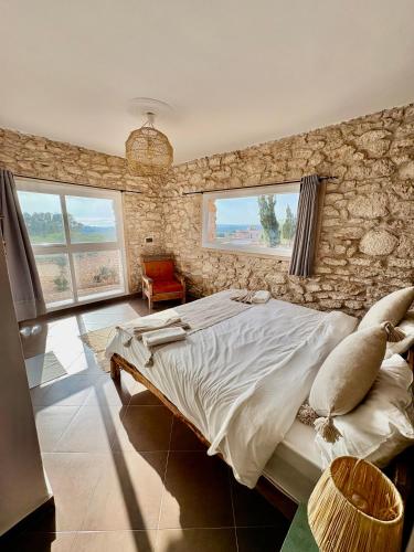 a bedroom with a stone wall with a bed and windows at Chez les copains in Sidi Kaouki