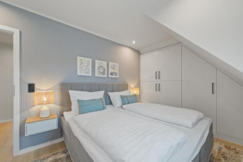a white bedroom with a large white bed with blue pillows at Nordseebude Deichtraum in Sankt Peter-Ording