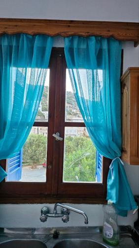 a window with blue curtains over a kitchen sink at Sea Breeze Retreat in Lionas