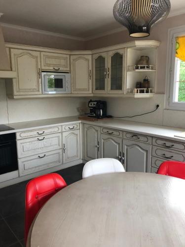 a kitchen with white cabinets and a table and red chairs at Gîte Aux Anges 51 in Thiéblemont-Farémont