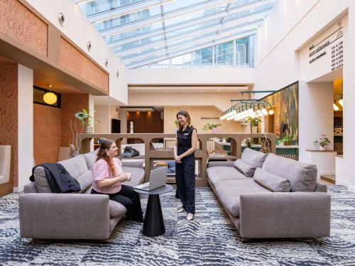 Zwei Frauen stehen in einer Lobby mit Sofas. in der Unterkunft Mercure Brussels Centre Rogier in Brüssel