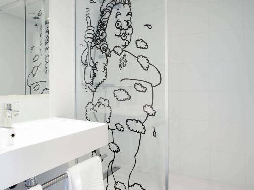 a bathroom with a black and white drawing on the wall at ibis Styles Nancy Sud in Houdemont