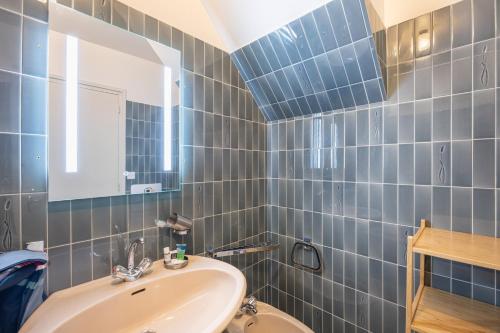 a blue tiled bathroom with a sink and a mirror at Gîte Le Lot in Espalion