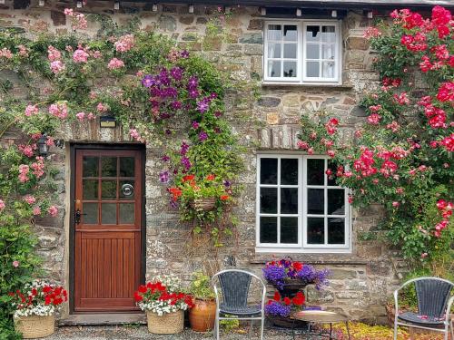 a stone house with flowers and a door and chairs at Little Forda in Chillaton