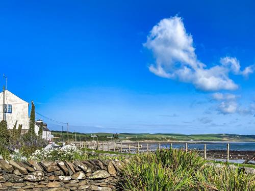 a beach with a building and a stone wall at Gigha in Drummore