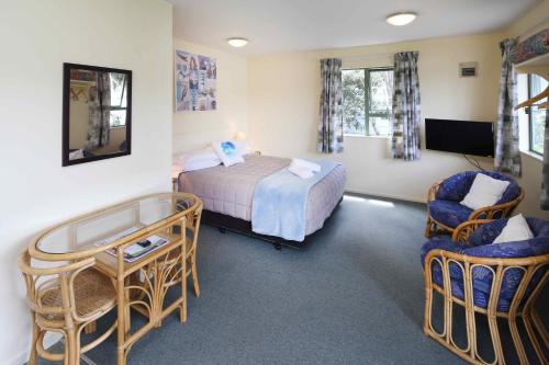 a bedroom with a bed and a desk and chairs at Waiheke Island Motel in Ostend