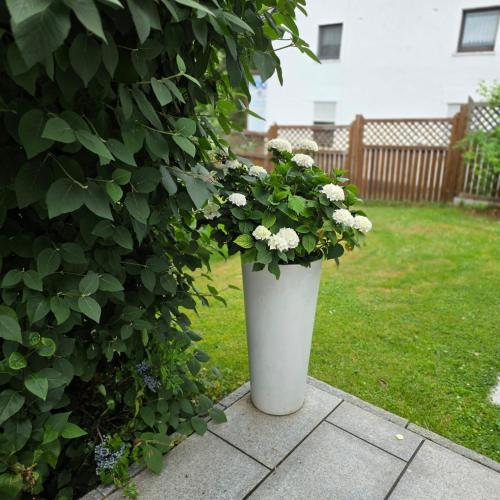 a white vase with flowers in it next to a bush at Ferienhaus Schwerte Ergste im Ruhrtal in Schwerte
