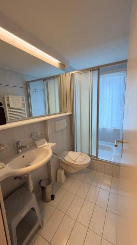 a bathroom with a sink and a toilet and a tub at Hotel Heilquelle-Leukerbad-Therme in Leukerbad