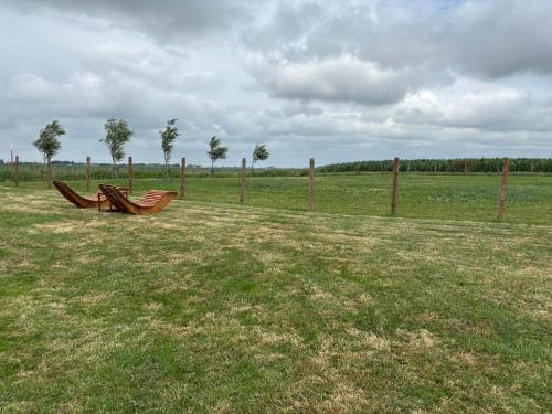 Zwei Holzbänke stehen auf einem Feld neben einem Zaun in der Unterkunft Vakantie appartementen Sylsicht in Sexbierum