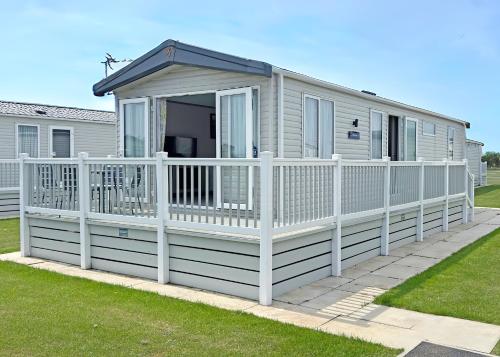 a mobile home with a porch and a white fence at Golden Anchor Caravan Park in Chapel Saint Leonards
