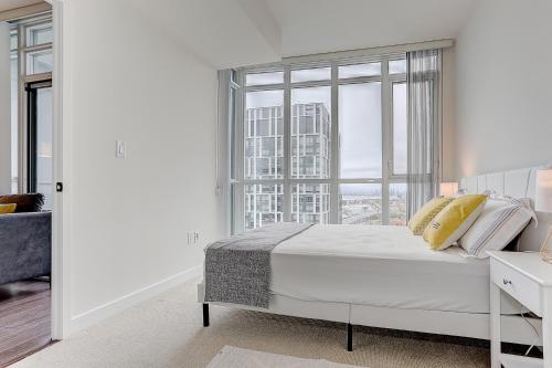 a white bedroom with a bed and a large window at Lakeview 1 Bed 1 Den by Rogers Centre in Toronto