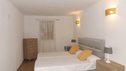 um quarto com uma cama com lençóis brancos e almofadas amarelas em Casa Rural Valdezaque em Cordobilla de Lácara