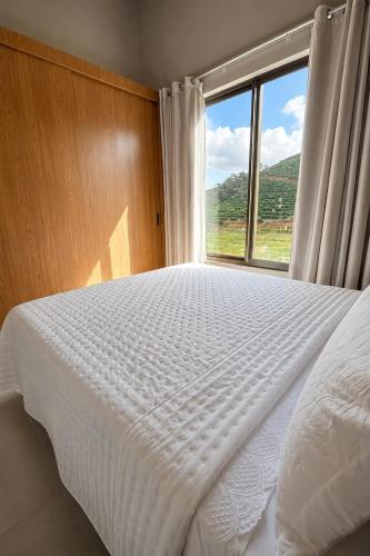 a bedroom with a white bed with a large window at Chalé 1 - Vivendas do Caparaó in Pedra Menina