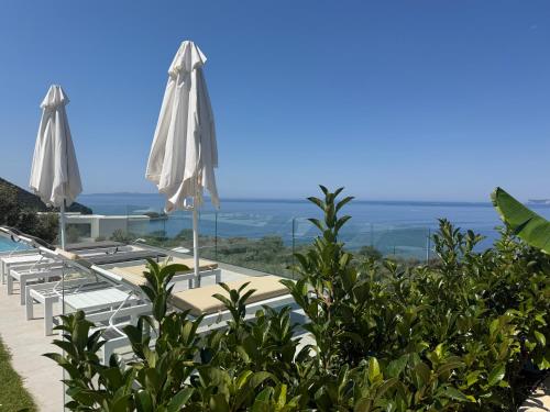 a pool with two white umbrellas and the ocean at Villa Veneti in Pérdika
