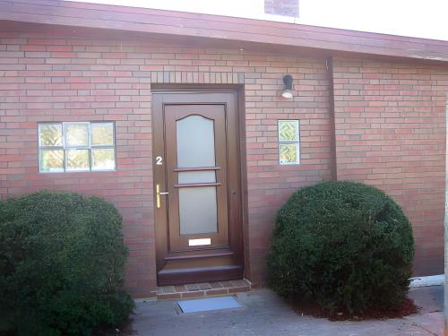 a brown door on a brick house with two bushes at Kajüte H-8 in Butjadingen