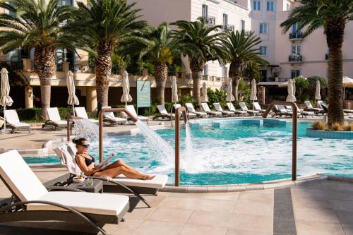 a woman sitting in a chair in front of a swimming pool at Thermae Sylla Spa & Wellness Hotel in Loutra Edipsou