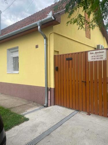 a yellow house with a wooden gate and a door at Tuba Apartman in Kiskunhalas