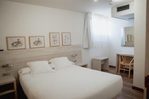 a white bedroom with a white bed and a table at Hostal Bertran in Salás de Pallás