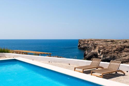 a swimming pool with two chairs and the ocean at VORAMAR by 3VILLAS in Cala en Forcat