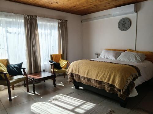 a bedroom with a bed and two chairs and a clock at Lourette se Plek in Sannieshof