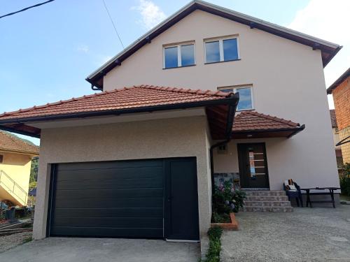 a white house with a black garage door at Kuća - Šekovići in Šekovići