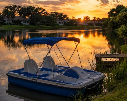 a blue boat sitting on the water at sunset at Splash & Relax Games WiFi BBQ Fire Pit Boat Lake in Royal Palm Beach