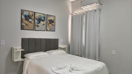 a white bedroom with a bed and a window at Hotel Lara - Simolândia in Alvorada do Norte 
