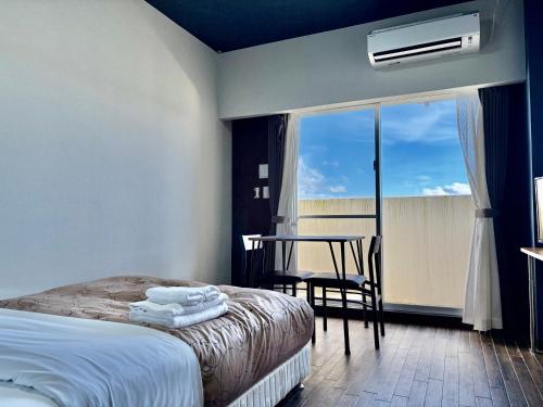 a bedroom with a bed and a table and a window at HOTEL Progress inn 名護 MATABee in Nago