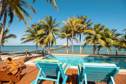 a swimming pool with two blue chairs and the ocean at Condo #23 @ Beachside Villas in Placencia