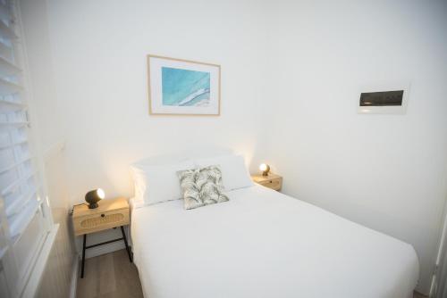 a white bedroom with a white bed and two night stands at Albany Central Apartments in Albany